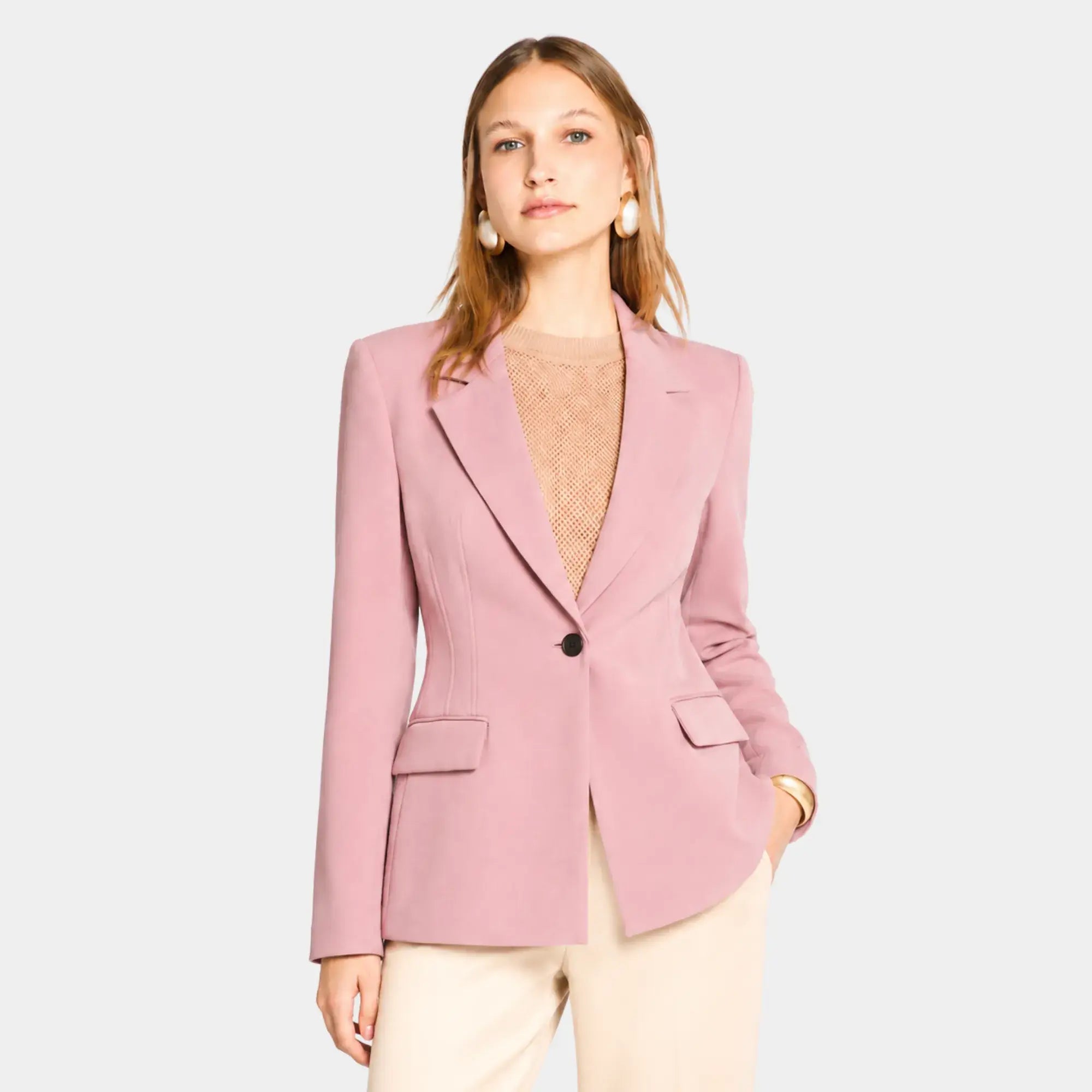 Mulher usando blazer feminino rosa de alfaiataria acinturado com botão único e calça clara elegante