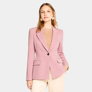 Mulher usando blazer feminino rosa de alfaiataria acinturado com botão único e calça clara elegante