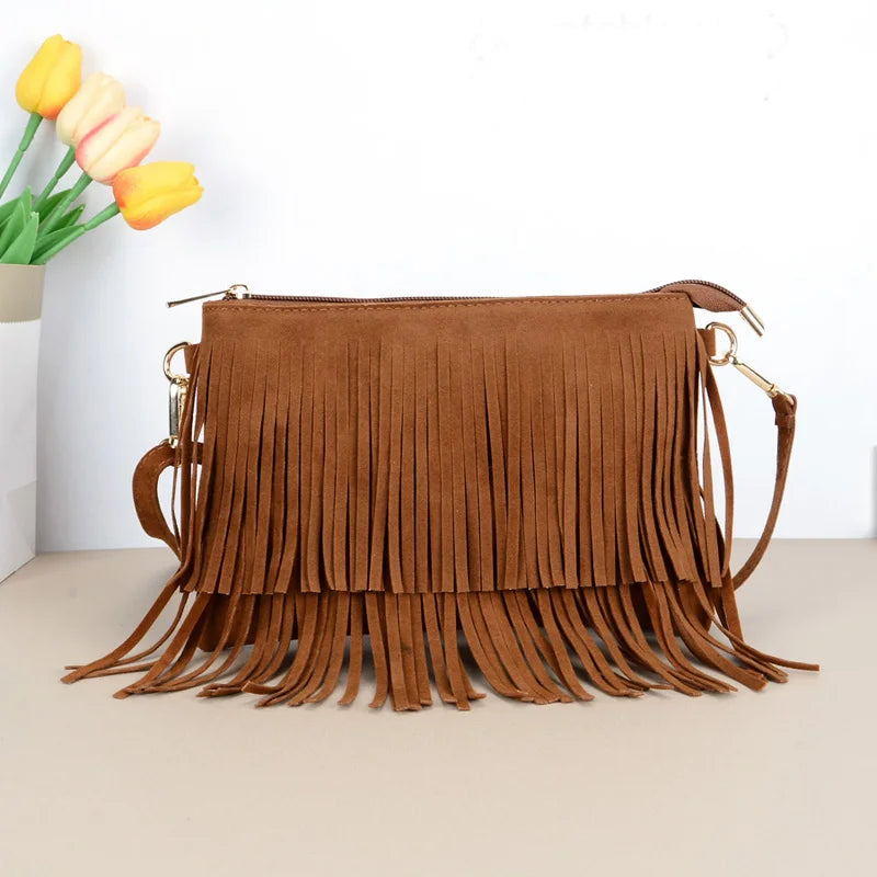 Bolsa crossbody de camurça caramelo com franjas na frente e alça longa, sobre fundo claro com flores
