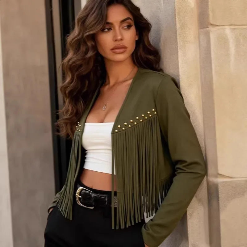 Modelo de jaqueta curta verde militar com franjas e tachas, top branco e cinto, diante de parede de pedra