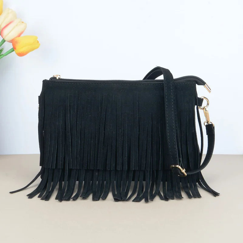 Bolsa crossbody de camurça preta com franjas na frente e alça longa, sobre fundo claro com flores