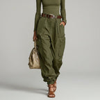Modelo de calça cargo wide leg verde militar de cintura alta com cinto marrom, blusa verde e bolsa bege