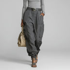 Modelo de calça cargo wide leg cinza chumbo de cintura alta com cinto, blusa cinza clara e bolsa bege