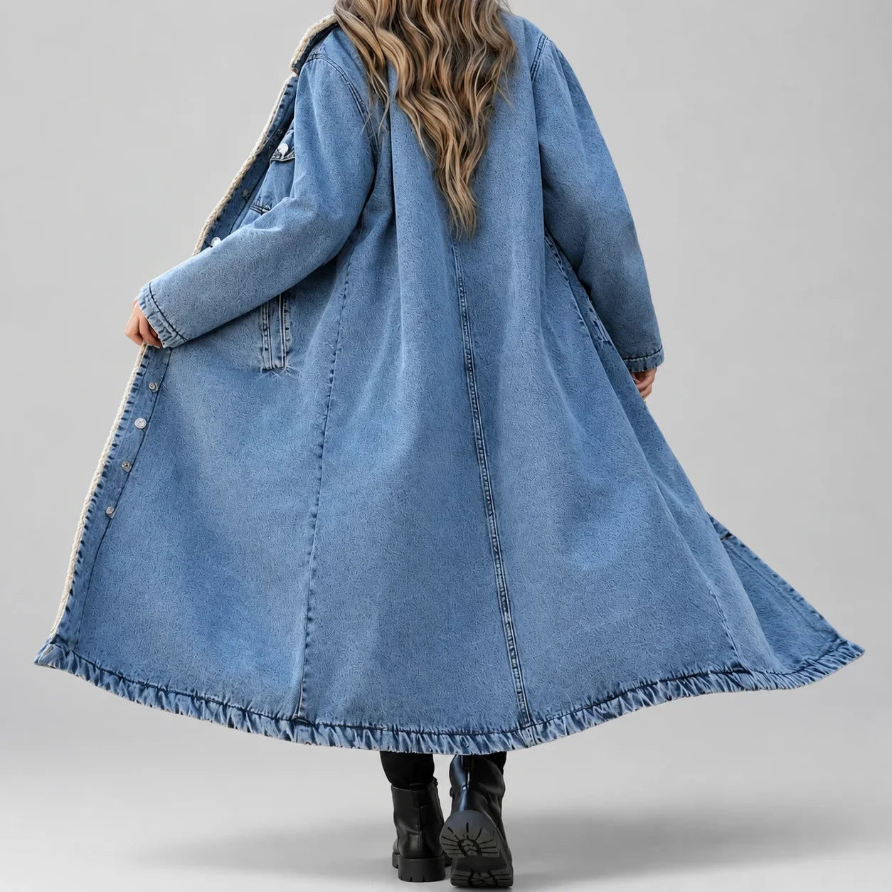 Modelo de costas com casaco longo jeans azul claro, mostrando o caimento amplo e a barra desfiada