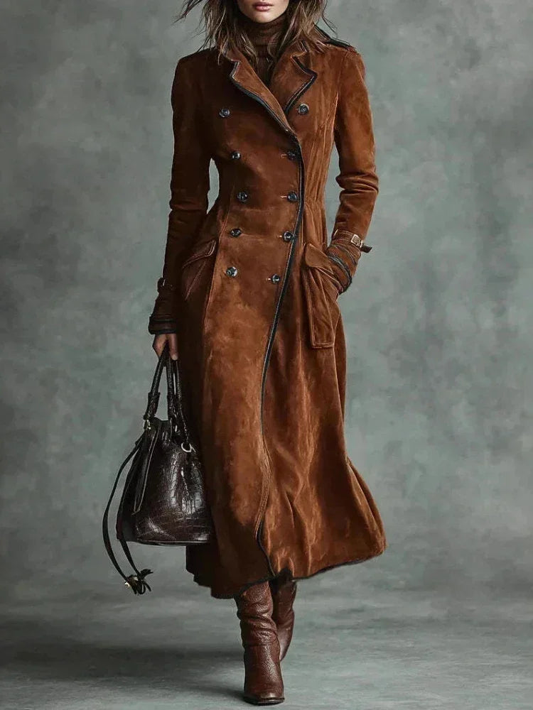 Modelo de trench coat longo de camurça marrom com bolsa de couro e bota de salto, em fundo cinza esverdeado
