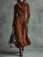 Modelo de trench coat longo de camurça marrom com bolsa de couro e bota de salto, em fundo cinza esverdeado